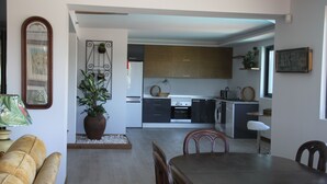 A modern kitchen with wooden cabinets, a dining area with a table and chairs, and a large potted plant. - Villas Marim Heron House  (Olhão)
