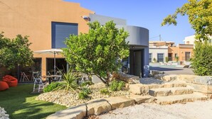 A modern building with a curved facade, outdoor seating area, and a well-maintained garden with rocks and a tree. - Villas Marim Heron House  (Olhão)