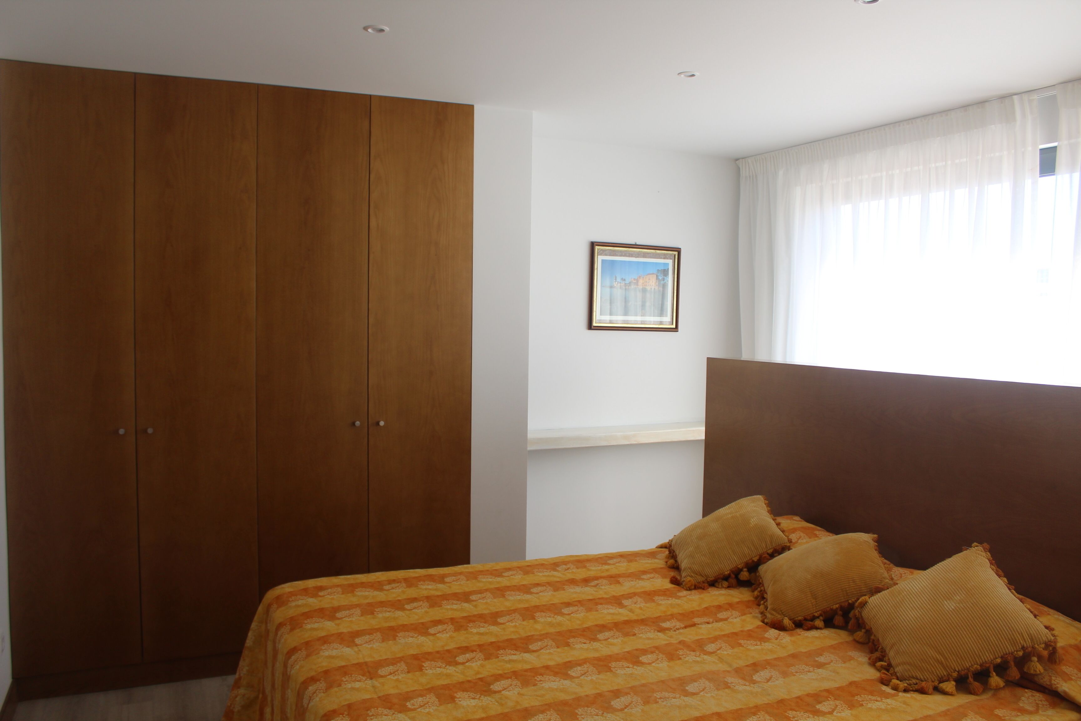 A bedroom with a large wardrobe, a bed with patterned bedding, and a window with curtains.