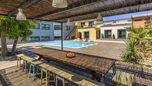 An outdoor pool area with a wooden deck, lounge chairs, and a dining table with fruit. - Villas Marim Heron House  (Olhão)