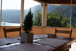 A wooden table with a potted plant, two chairs, and a view of mountains and water through a window.