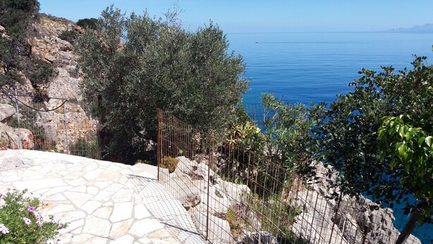 Une zone pavée de pierres, délimitée par une clôture métallique, qui offre une vue sur une côte rocheuse et la mer.