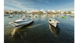 Un port de plaisance avec plusieurs bateaux amarrés, un ciel dégagé et des bâtiments en arrière-plan.