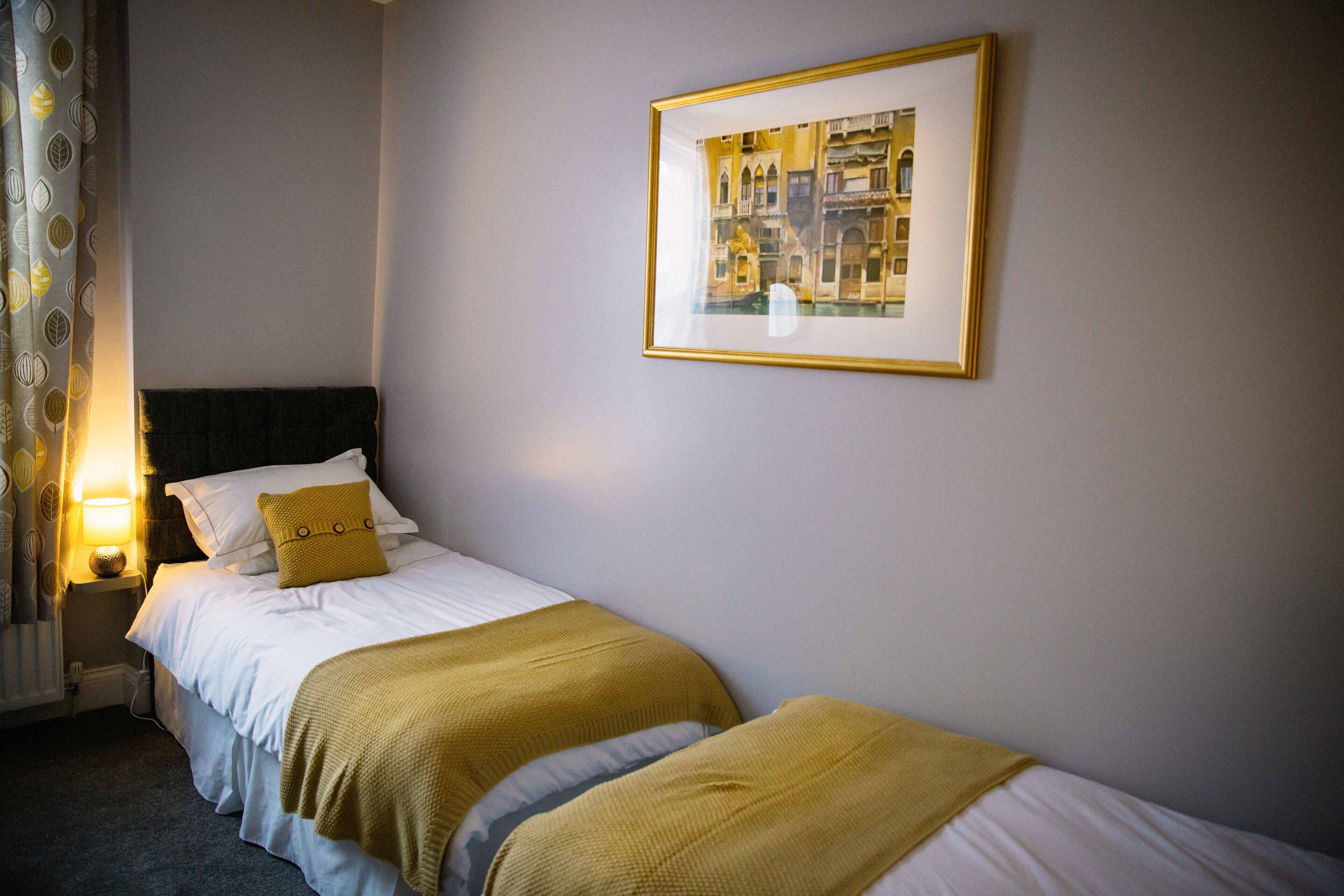 A hotel room with two beds, a framed picture on the wall, and a nightstand with a lamp.