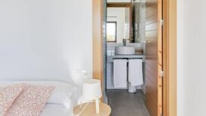 Un dormitorio con una cama, un taburete pequeño y una mesita de noche.