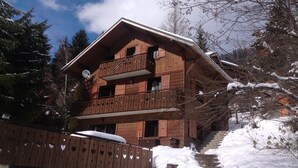 Un chalet en bois doté d’un balcon et d’une antenne parabolique, entouré de neige et d’arbres.