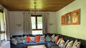 Un salon avec un canapé gris foncé, plusieurs coussins à motifs, une table basse en bois et un lustre.