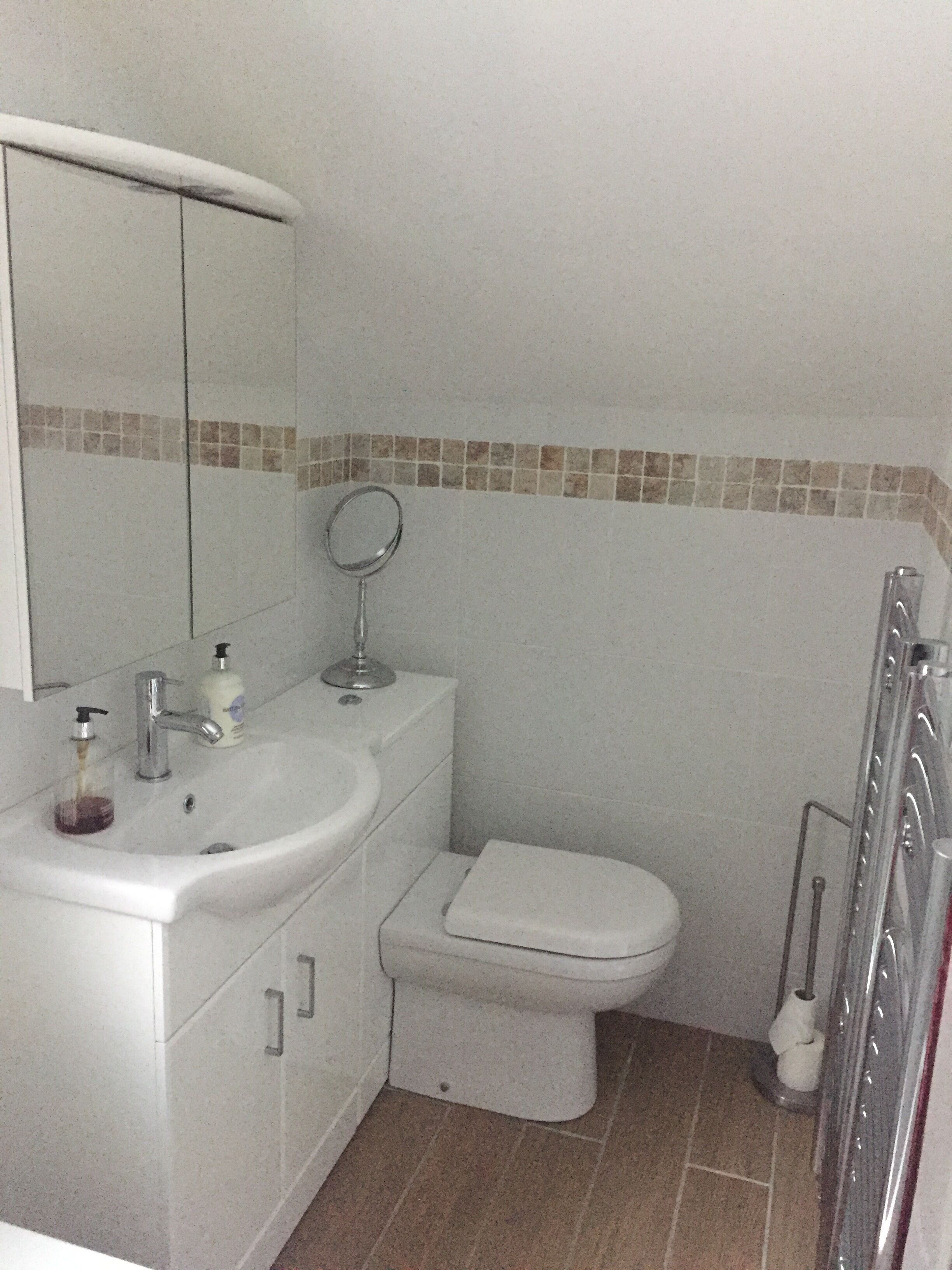 A bathroom with a white sink, mirror, and toilet. There is a shower area with a glass door.