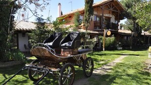 Een rustieke houten huwagen met leren stoelen, geparkeerd in een tuin.