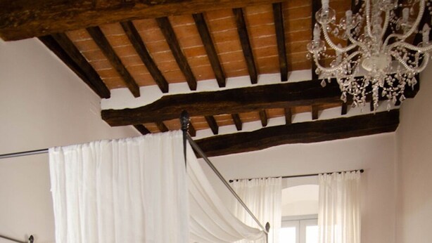 Une chambre à coucher avec un lit à baldaquin, un banc, un lustre et une fenêtre avec des rideaux.