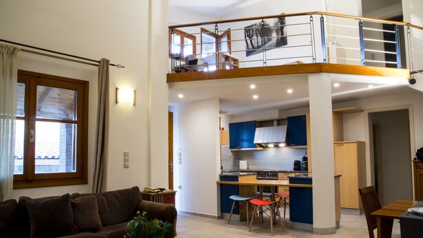 Amplia sala de estar con una mesa de centro de vidrio, un sofá marrón y una mesa de comedor con sillas. Se ve una cocina al fondo, con gabinetes azules y una encimera de madera.