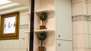 Un baño con tragaluz, estantes blancos con plantas en macetas, un espejo y un armario.