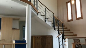 Amplia sala de estar con escalera que conecta dos plantas, armarios de madera, una mesa de comedor y zona de cocina.