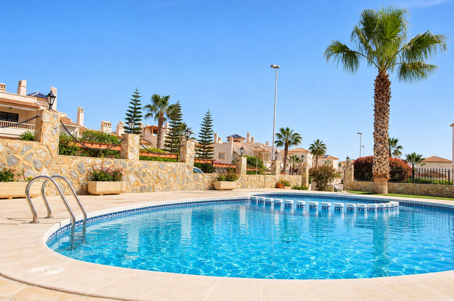 A swimming pool with a stone wall and palm trees.