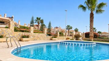A swimming pool with a stone wall and palm trees.