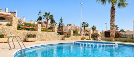 A swimming pool with a stone wall and palm trees.