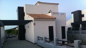 Un edificio moderno con techo de tejas, entrada protegida y fachada plana.