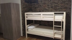 Una cama litera en una habitación con pared de piedra y un armario.