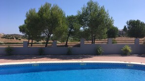 Una piscina con borde de azulejos, rodeada por un muro bajo y pequeñas plantas.