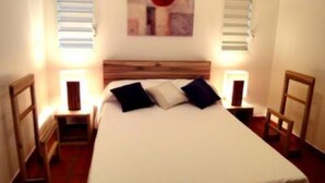 A neatly made bed with a wooden headboard, two bedside tables with lamps, and a painting above the bed. - House / Villa - SAINT FRANçOIS (Saint François)