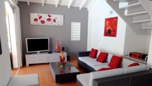 A modern living room with a grey sofa, red cushions, a flat-screen TV, and a staircase. - House / Villa - SAINT FRANçOIS (Saint François)