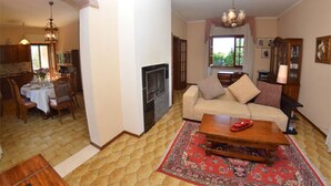 A living room with a sofa, coffee table, and a fireplace. There is a dining area with a table and chairs. The room has a tiled floor and a large window. - Villa with private pool in Lucca, special offers! (Capannori)