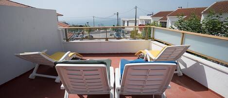 A rooftop terrace with white lounge chairs and a table, overlooking a cityscape.