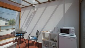 En lille balkon med et bord og stole, en mikrobølgeovn og en reol med service.