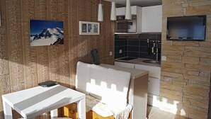 Een moderne keuken met houten lambrisering, een eethoek met een witte tafel en stoel, en een accentmuur van steen.