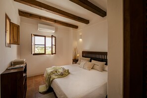 Une chambre à coucher comprenant un lit, des poutres en bois, un appareil de climatisation, une fenêtre, une table de chevet et une commode.