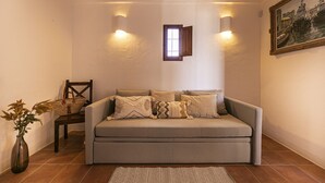 Un salon confortable avec un canapé, un fauteuil, une petite fenêtre et un tableau accroché au mur.