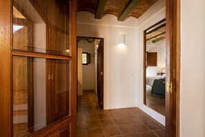 Un couloir avec des portes en bois et un sol carrelé qui mène à une chambre à coucher, où se trouvent un lit et une table de chevet.