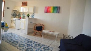 Un espacio habitable compacto con kitchenette, un área de comedor con una silla y mesa, y una alfombra colorida.