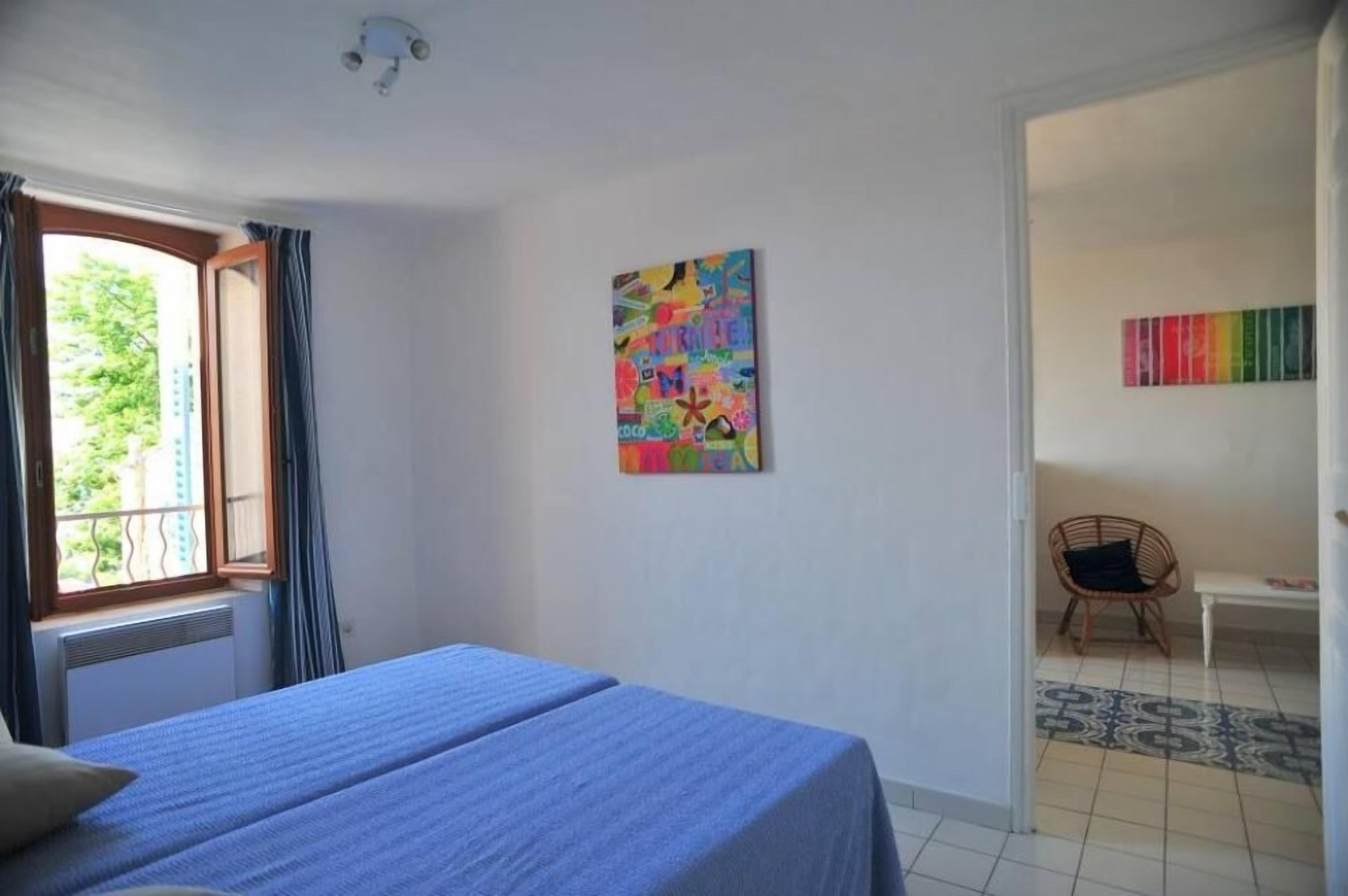 Una habitación con una cama, un cuadro abstracto de colores, una silla y una pequeña mesa.