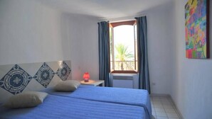 Un dormitorio con dos camas, una mesita de noche con lámpara, una ventana con cortinas y un cuadro llamativo en la pared.