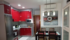 A modern kitchen with red cabinets, stainless steel appliances, and a dining area with a table and chairs.