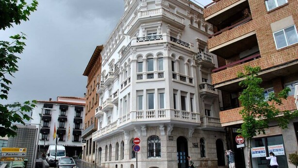 A corner building with a white facade, a visible entrance, and a sign indicating a hotel.
