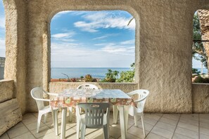Een terras met een tafel en stoelen, uitzicht op de zee en een stenen muur.