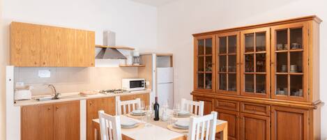 A compact kitchen with wooden cabinets, a dining table with chairs, and a built-in cabinet with glass doors.