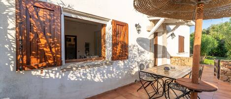 A patio with a table and chairs, a wicker umbrella, and a window with wooden shutters.