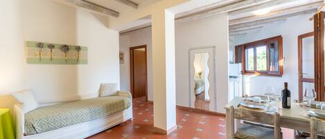 A cozy room with a bed, a dining table set for two, and a kitchen area visible through an open door.