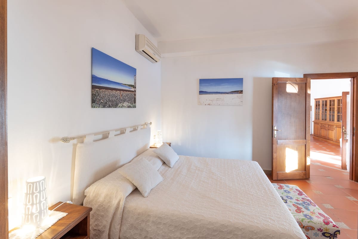 Een slaapkamer met een groot bed, een nachtkastje, twee wandairconditioners en twee ingelijste foto's.