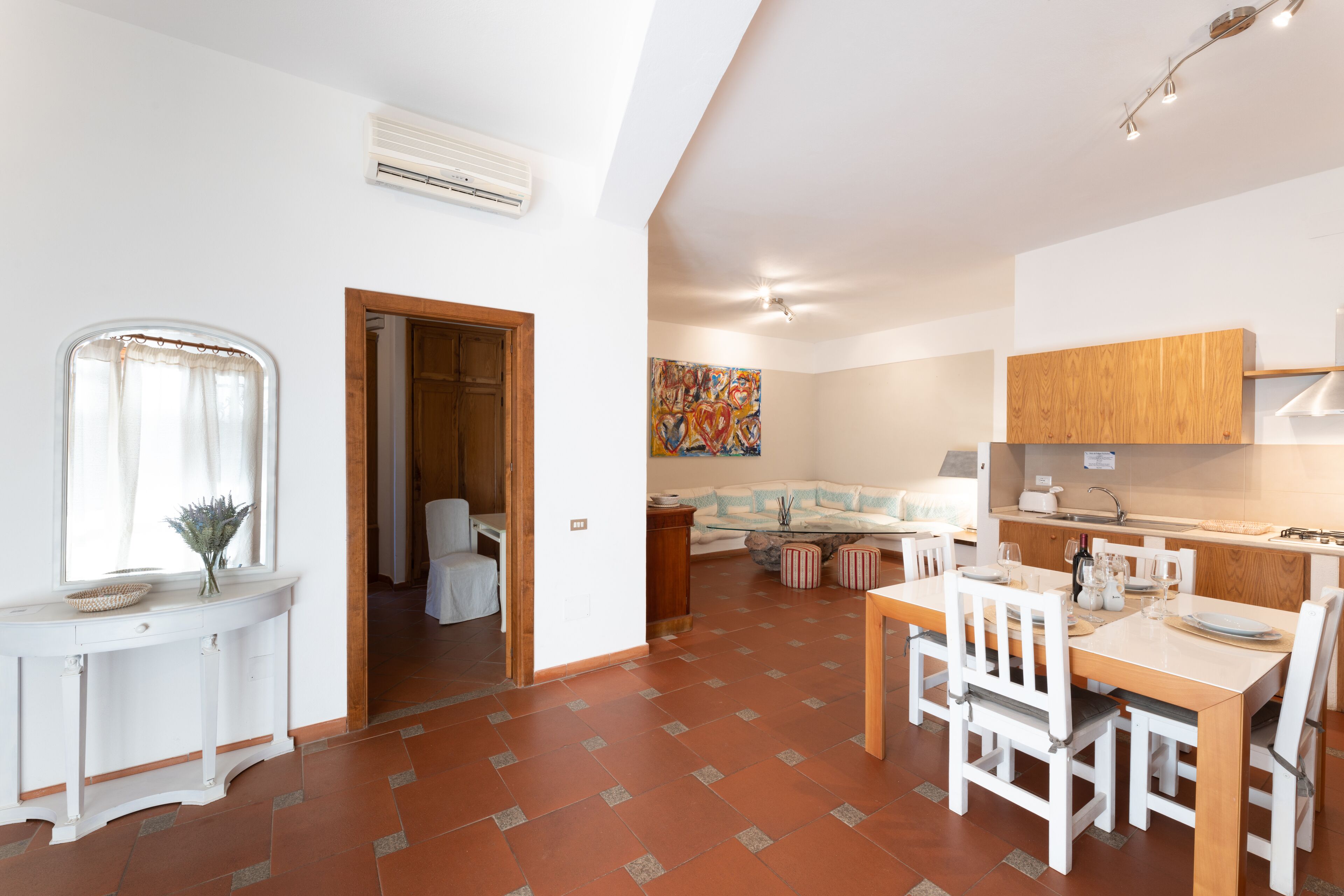 A spacious living area with a dining table, chairs, and a kitchen area with wooden cabinets and a tiled floor.