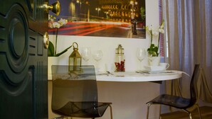 Un comedor con una mesa dispuesta para dos, un jarrón de flores y un cuadro con una vista urbana.