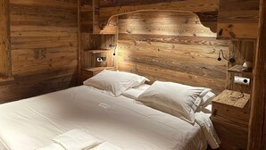 A wooden cabin-style bedroom with a bed, pillows, a nightstand, and a wall-mounted lamp.