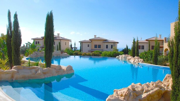 Una piscina rodeada de villas de estilo mediterráneo bajo un cielo azul cristalino.