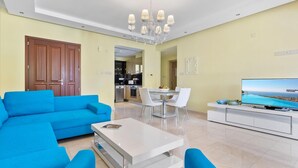 Una sala de estar moderna con un sofá azul, una mesa de centro blanca y un televisor sobre un mueble blanco.