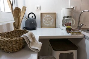 A kitchen with a kettle, wooden utensils, a coffee maker, and a framed sign.