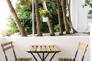 A wooden table with two chairs, surrounded by trees and potted plants.