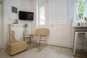 A room with a television mounted on the wall, a wicker rocking chair, a small table with a plant, and a white door.